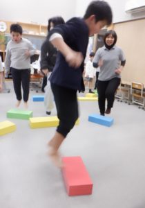 踏み台に向かって両足でジャンプする利用者様たちと職員